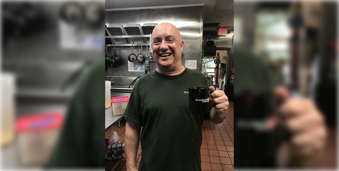 A man smiling in a kitchen taking a selfie with a mug.
