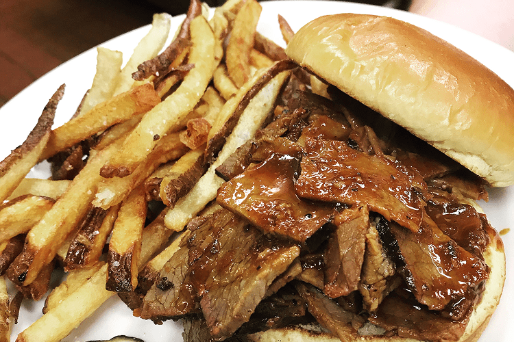 Barbecue beef sandwich with fries on plate.